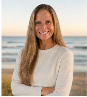 Smiling woman with long blonde hair standing by the beach at sunset.