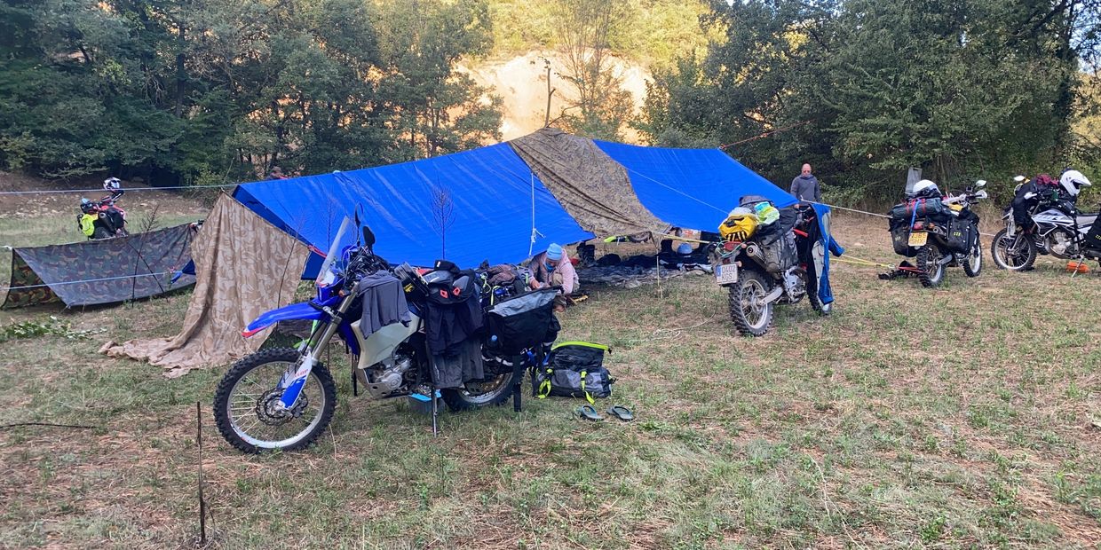 Motorcycles and a large blue tarp shelter in a forest clearing.