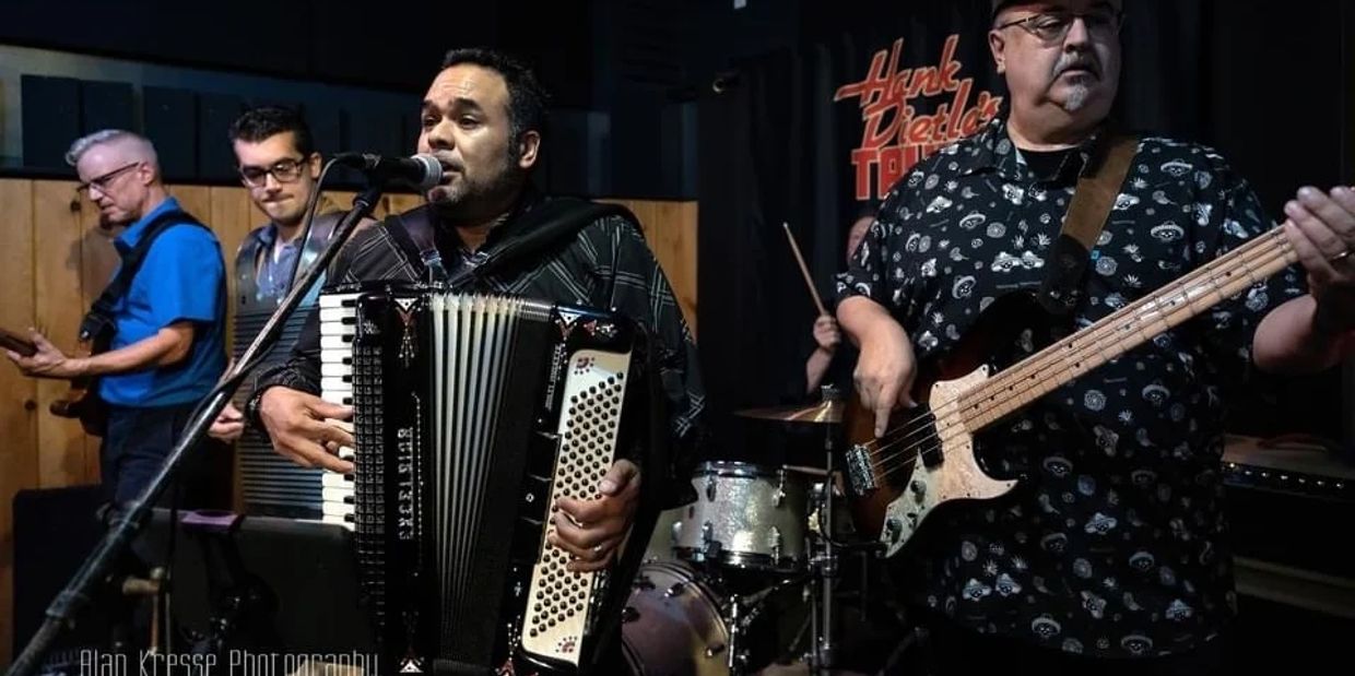 A band performs live with accordion, bass, guitar, and drums on stage.