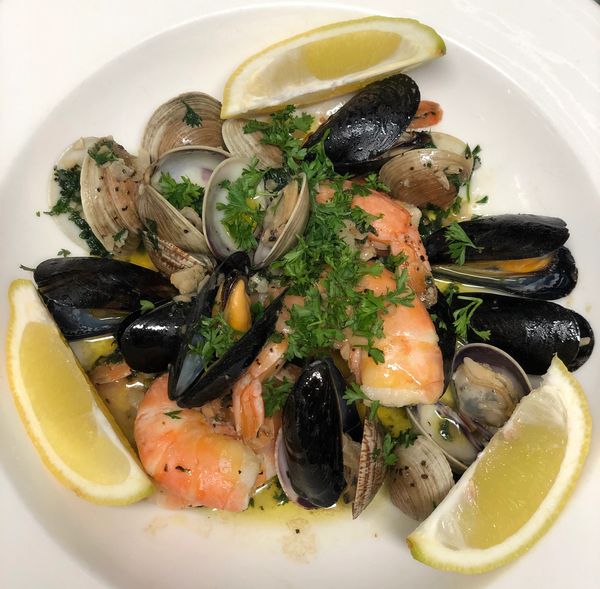 Seafood dish with shrimp, clams, mussels, herbs, and lemon wedges.