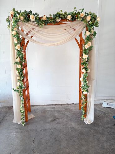 Beautiful wooden garden lattice arch with flowers and greenery with sheer drapery.