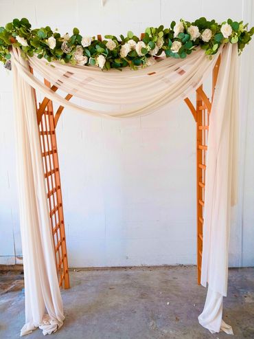 Garden lattice decorated with white flowers, greenery and champagne sheer drapery.
