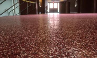 Close-up of a speckled red floor in a dim hallway leading to a bright exit door.