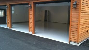 Empty double garage with polished concrete floors and wooden exterior.
