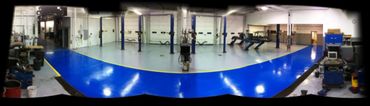 A clean, spacious automotive workshop with blue and gray flooring and vehicle lifts.
