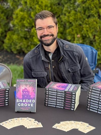Author smiling behind a table of his books titled 'Shaded Grove'.
