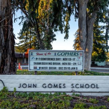 Entrance sign of John Gomes School with event dates.