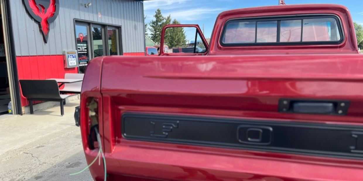 Red Ford pickup truck with missing tail light at a garage.