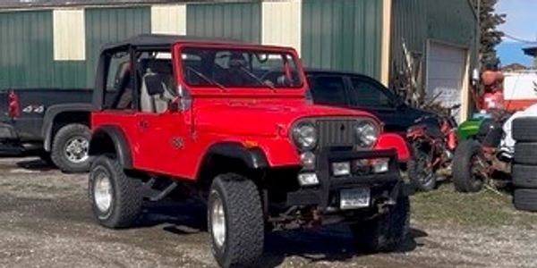 Red Jeep parked in front of a shed under a clear sky.