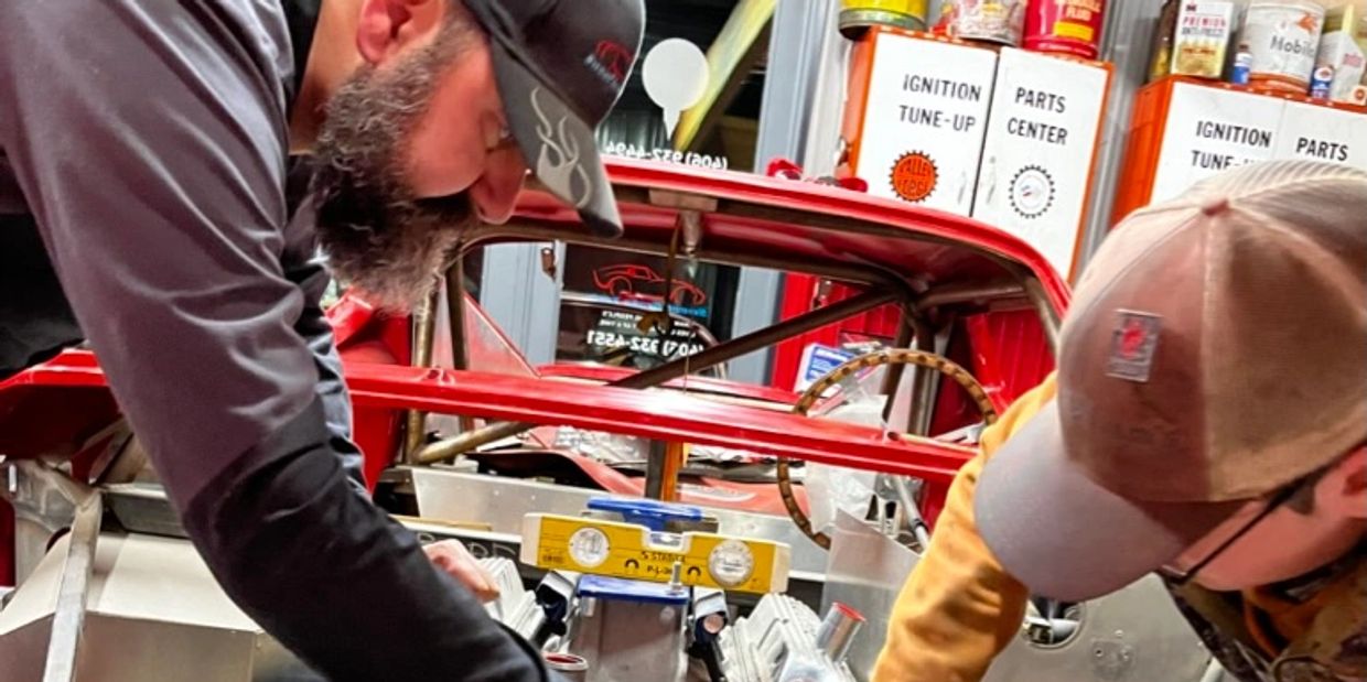 Two men working on a car engine inside a garage.