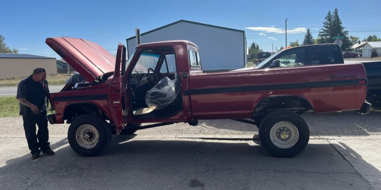 Man inspecting a vintage red pickup truck with hood and door open.