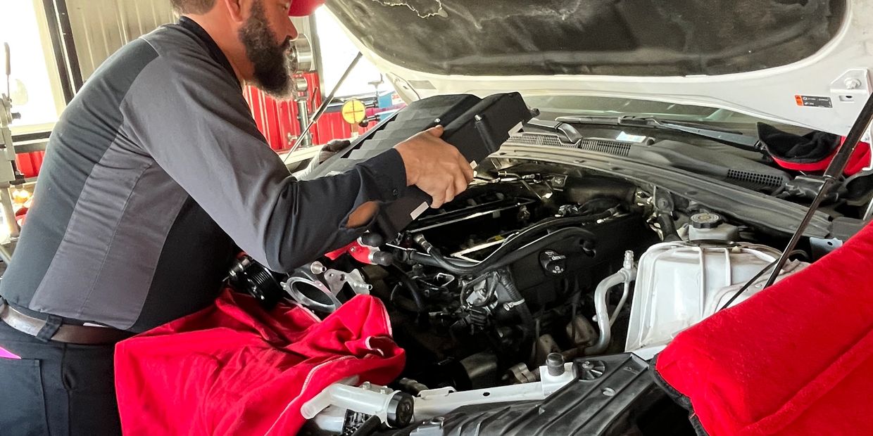 Mechanic working under car hood with a red cap.