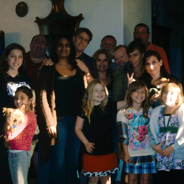 Group photo of smiling adults and children indoors, one child holding a small dog.