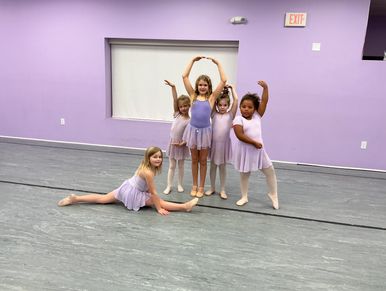 Five young girls in lavender ballet outfits posing in a dance studio.