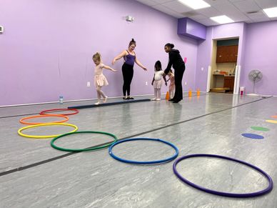 Children and instructors practicing ballet in a studio with colorful hoops on the floor.