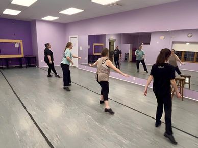 A group dance class practicing tap steps in a studio.