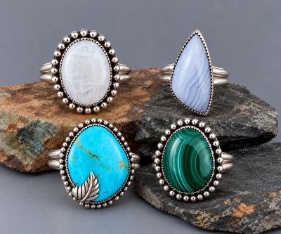 Four handcrafted sterling silver gemstone rings displayed on natural stones, featuring moonstone, bl