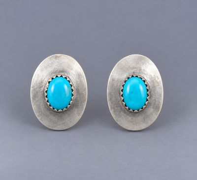 Pair of oval sterling silver post earrings with small bright blue turquoise stones centered in serra