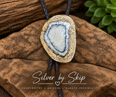 Dendritic agate bolo with hammered mixed-metal setting on black braided leather cord, displayed on r