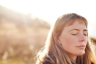 A woman with closed eyes enjoying sunlight outdoors.