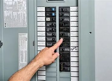 Person pointing at a circuit breaker panel inside an electrical box.