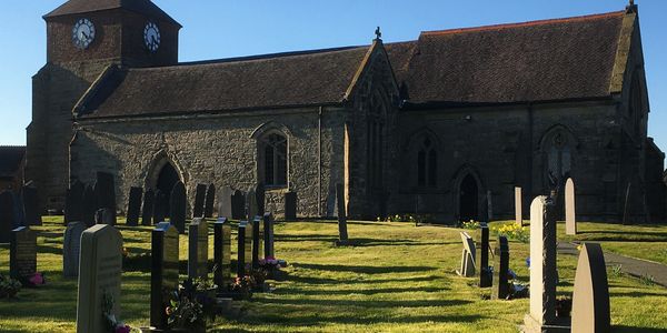 Historic stone church with clock tower and adjoining graveyard under clear sky.