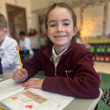 Student smiling, sitting at her desk from St. Thomas St. Timothy, West Hartford, CT.