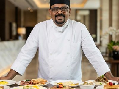 Smiling chef standing behind a table full of diverse dishes in a restaurant.