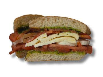 A sandwich with cheese, tomato, and pesto sauce on whole grain bread.