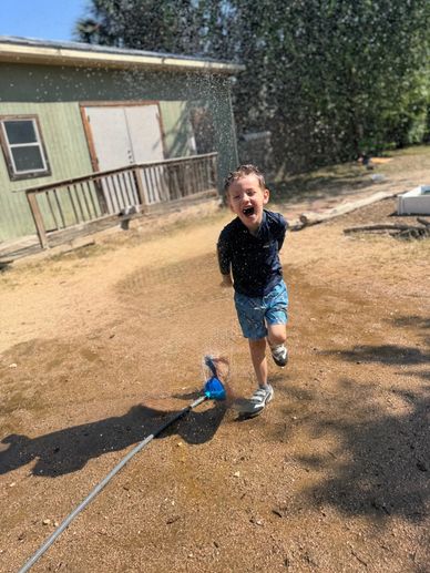 A young boy joyfully runs through a sprinkler on a sunny day.