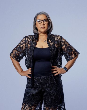 Confident woman with gray hair wearing glasses and a black lace top.