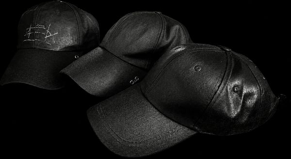 Three black leather baseball caps arranged in a row on a black background.