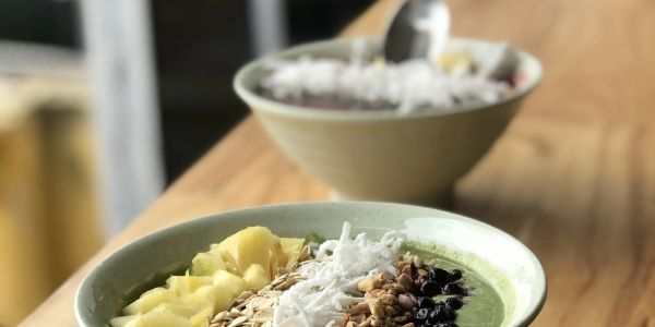 Two smoothie bowls topped with fruit, oats, and coconut flakes on a wooden table.
