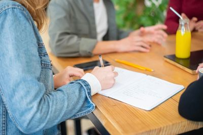 Person writing notes at a table during a meeting or study session.