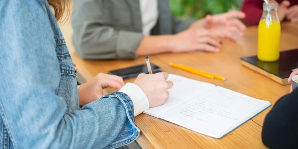 Person writing notes during a meeting at a wooden table.