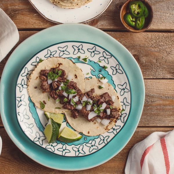 two beef tacos on blue plates with lime wedges