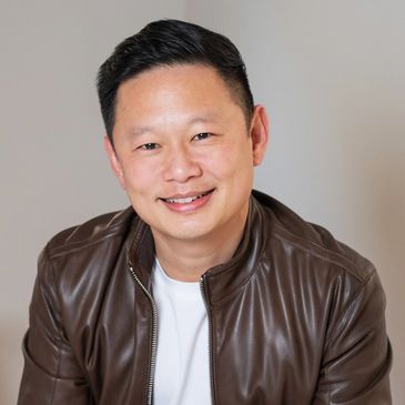 Smiling man in a brown leather jacket against a neutral background.