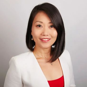 Smiling woman with straight black hair wearing a white blazer and red top.