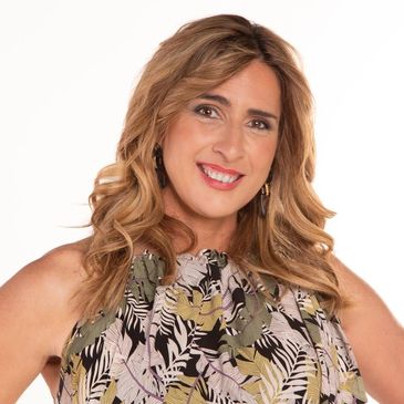 Smiling woman with wavy blonde hair wearing a patterned sleeveless top.