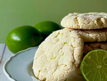 Lime cookies stacked on a plate with fresh limes in the background.