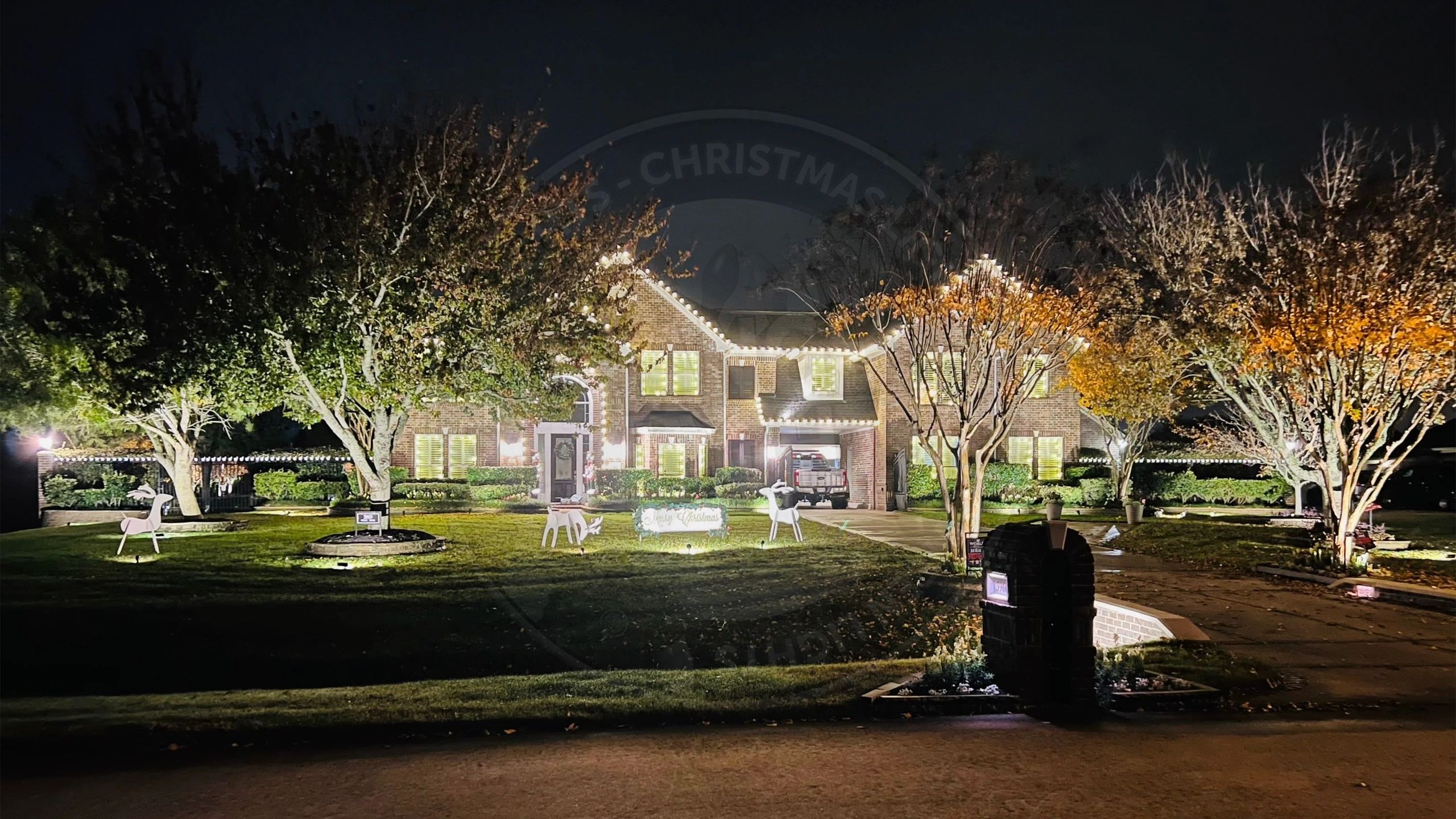 Large brick home with warm white C9 LED Christmas lights and reindeer yard decorations.