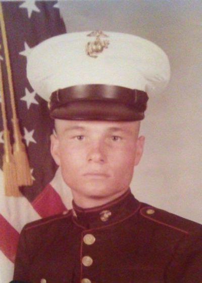 Portrait of a young Marine in dress uniform with American flag backdrop.