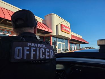 A patrol officer stands near a Circle K store under clear blue skies.