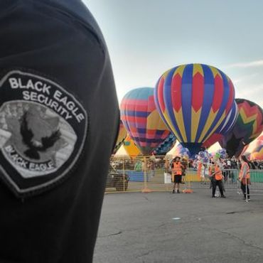 Security personnel oversee colorful hot air balloons at an outdoor event.