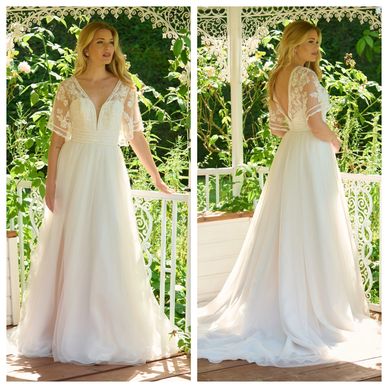 Elegant wedding dress with lace sleeves and flowing skirt in outdoor setting.