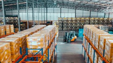 Large warehouse with stacked boxes and forklifts in wide aisles.