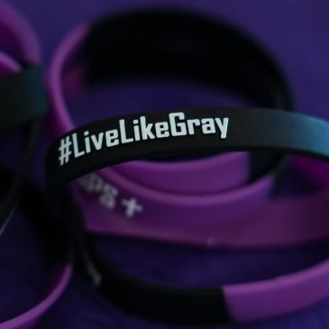 Black bracelet with #LiveLikeGray text on purple background.