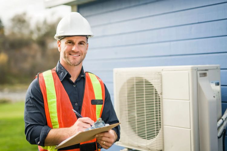 Technician in safety gear inspecting an outdoor air conditioning unit with a clipboard.