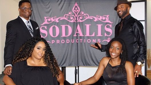 Four people posing in front of a Sodalis Productions banner, smiling.