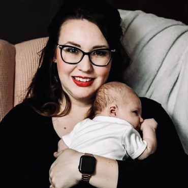 A smiling woman holding a newborn baby in a cozy chair.